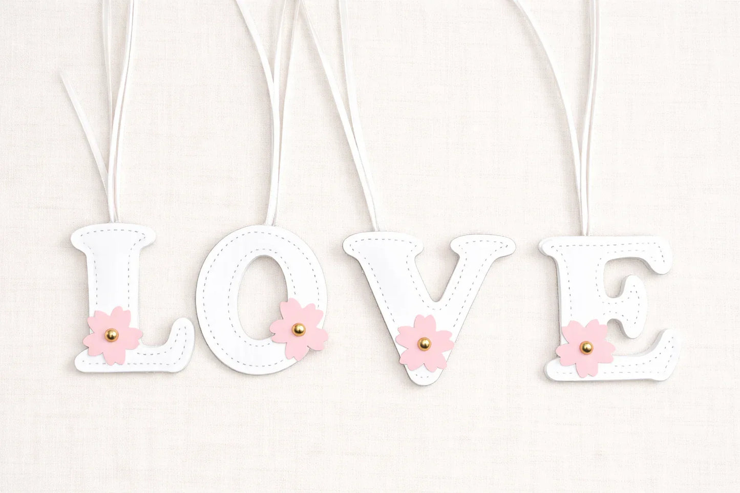 Initials in Bloom Alphabet Bag Charms spelling LOVE with leather strap on white backdrop.