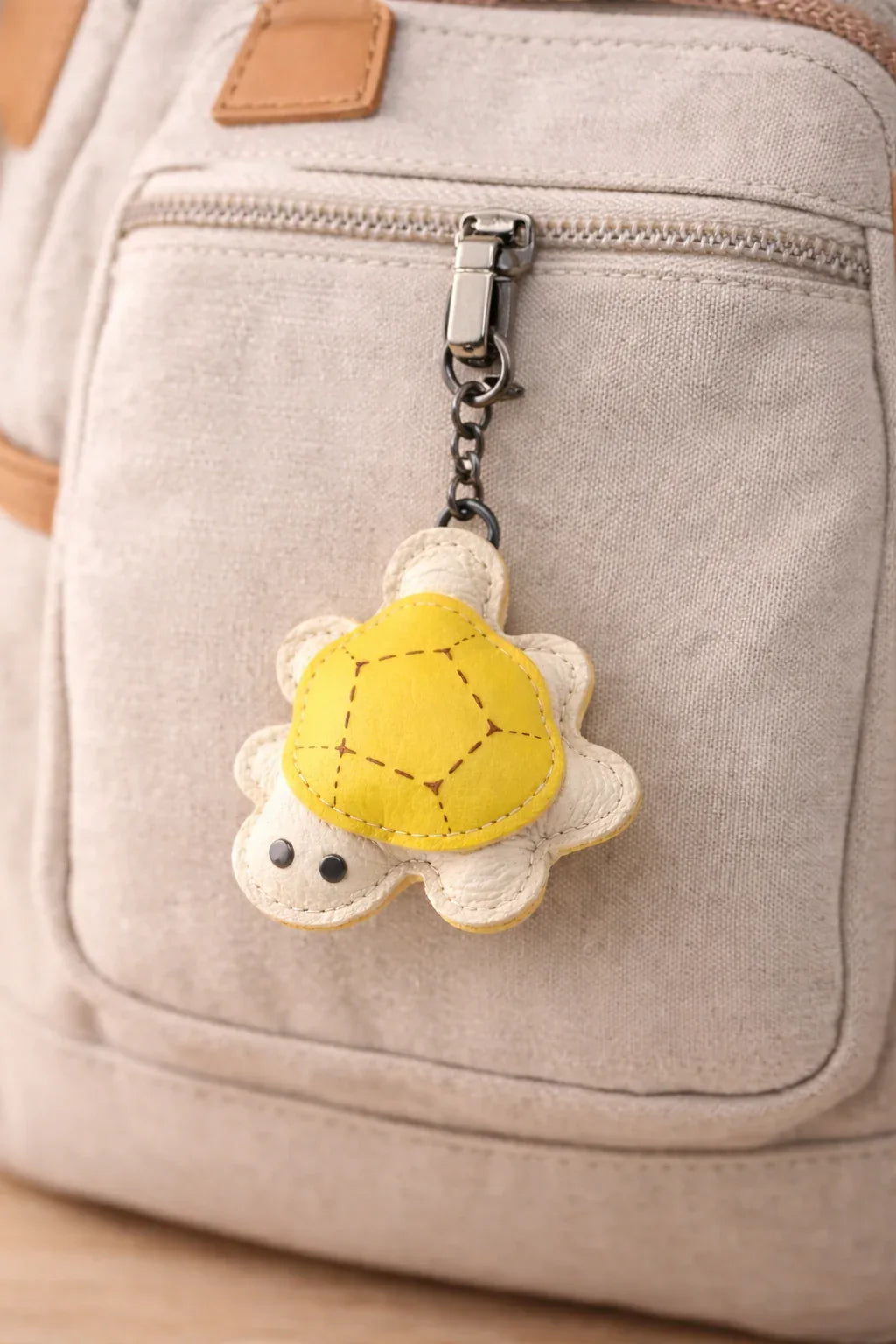 Yellow leather turtle key chain on tan backpack to show size and look.