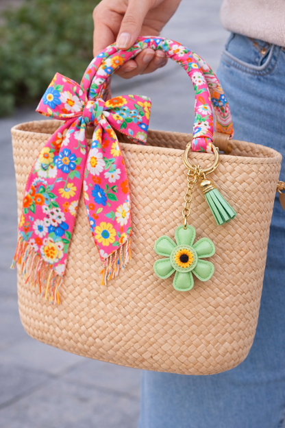 Green leather flower bag charm styled on a straw summer tote bag.