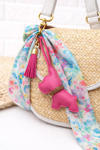 Pink colored  Pocket Puppy Leather Bag Charm  with collar on a straw purse with scarf. 