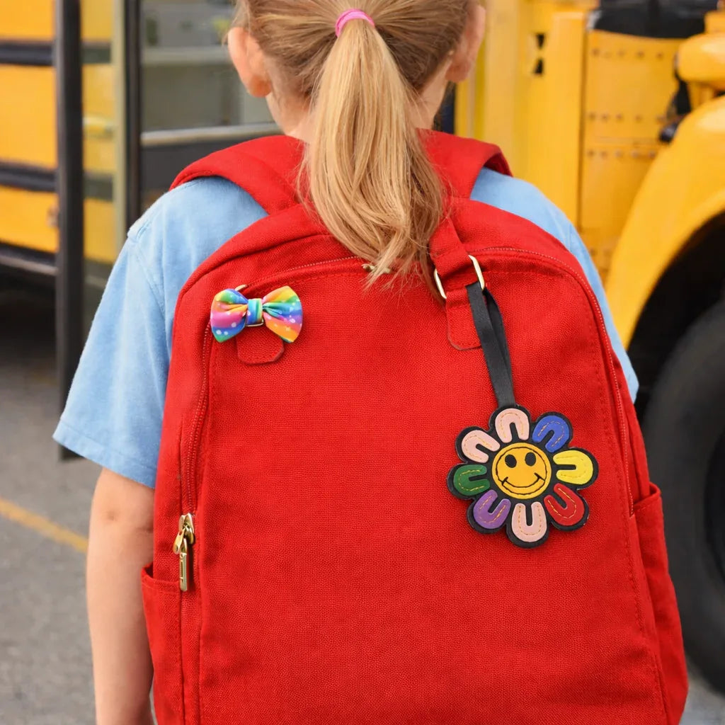 Child walking to bus with a multi colored  Smiles in Bloom Daisy Bag Charm on an orange backpack. 