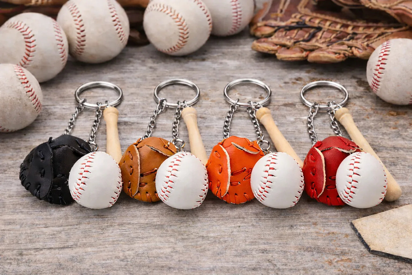 4 Baseball glove, ball and bat key chains on a table with baseballs and gloves to show size. 