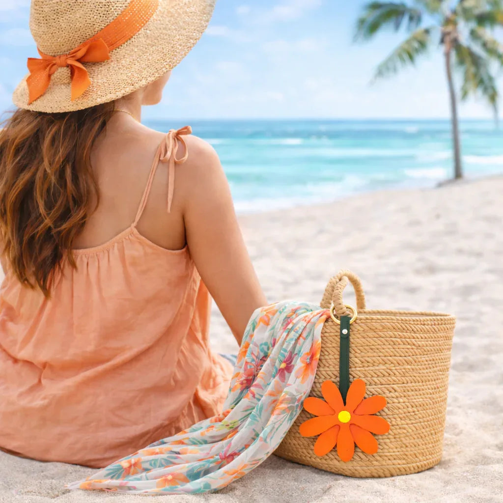 Woman on Beach with Coral Petal Pop Bag Charm on a straw bag with scarf. 