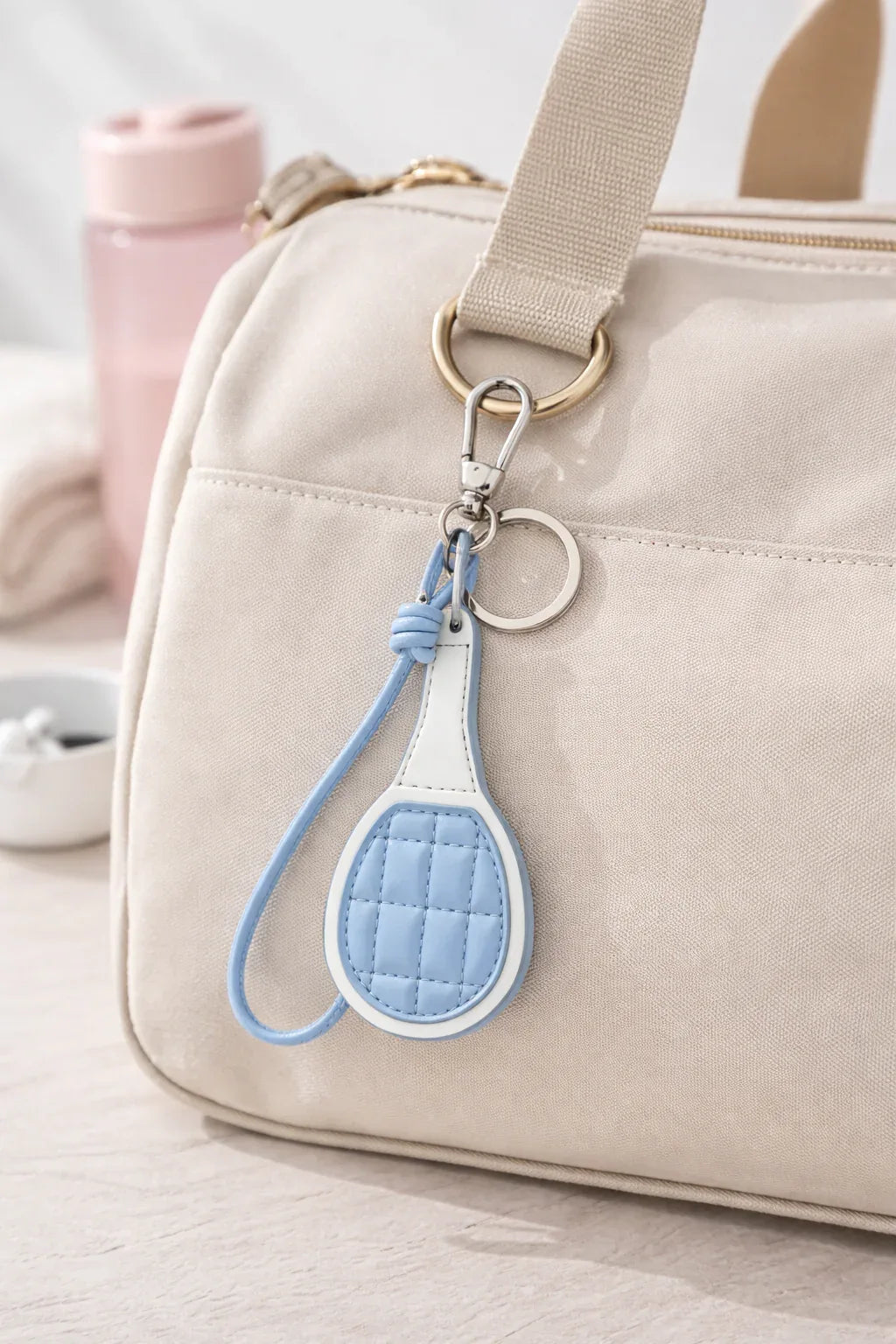 Beige gym bag with light blue pickle ball paddle key chain attached.