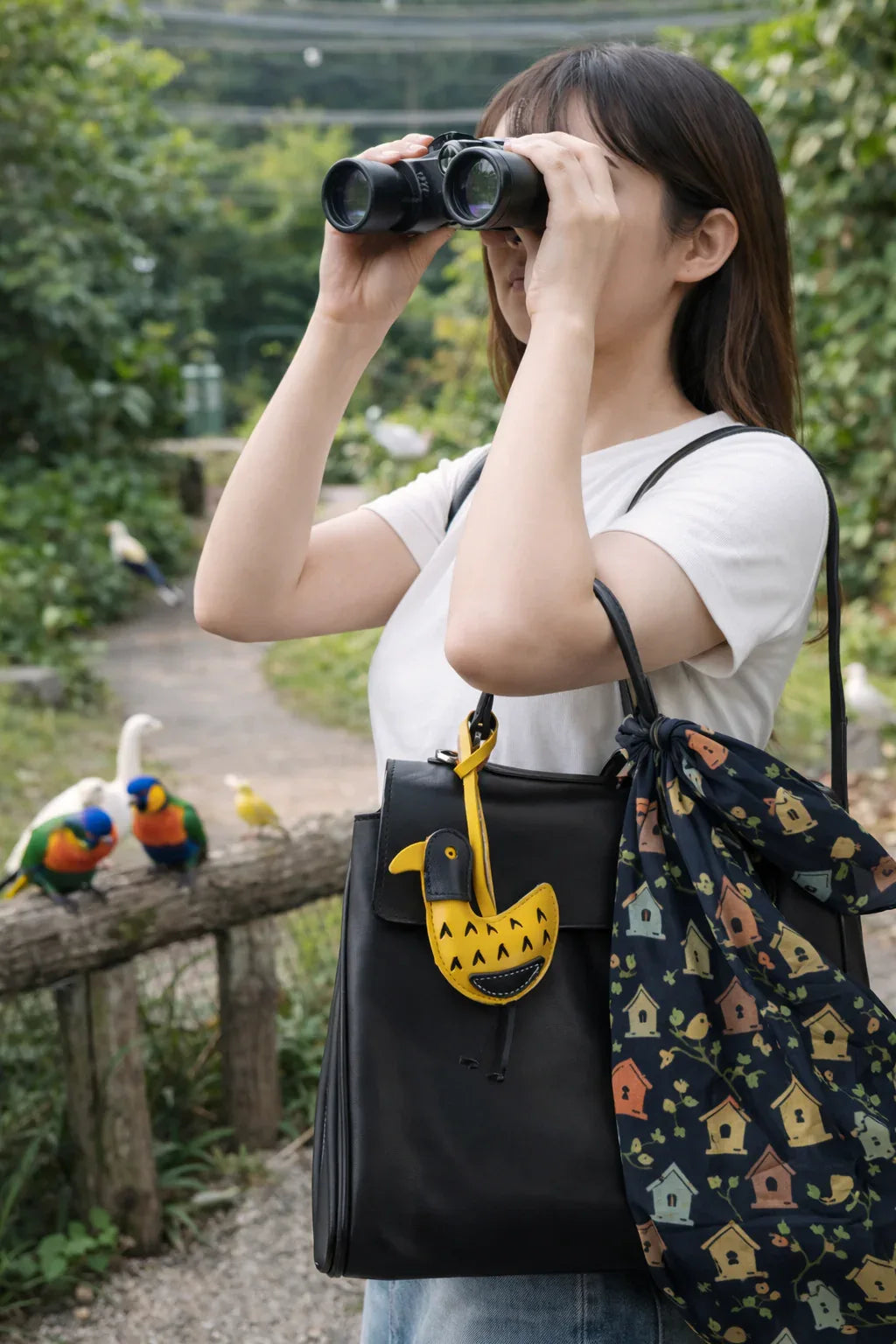 Women holding black bag with Golden Yellow Feathered Friend Leather Bag Charm while looking through binolculars outside. 