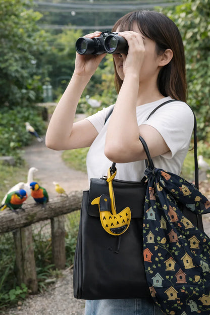 Women holding black bag with Golden Yellow Feathered Friend Leather Bag Charm while looking through binolculars outside. 