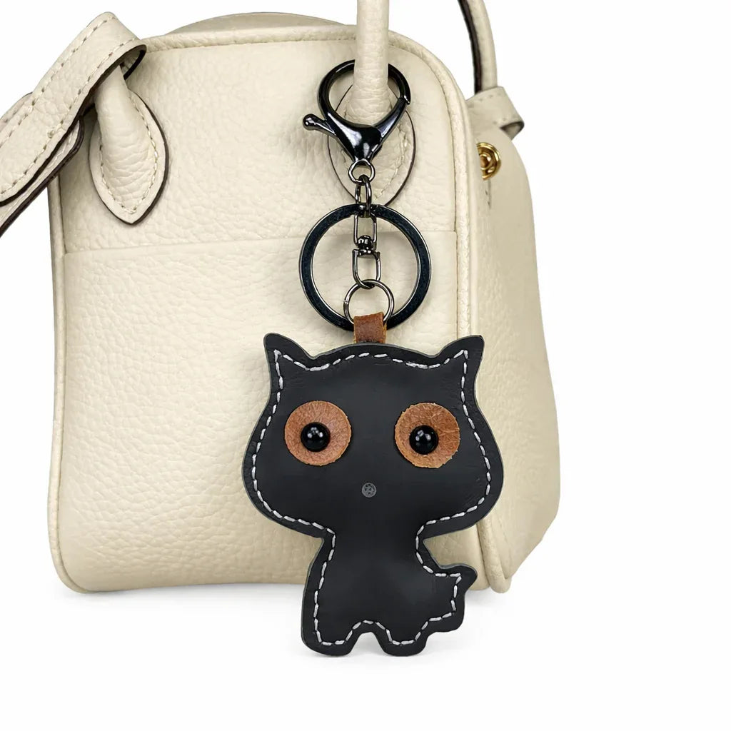 Whisker Wink black leather cat charm attached to the handle of a white  leather tote bag.