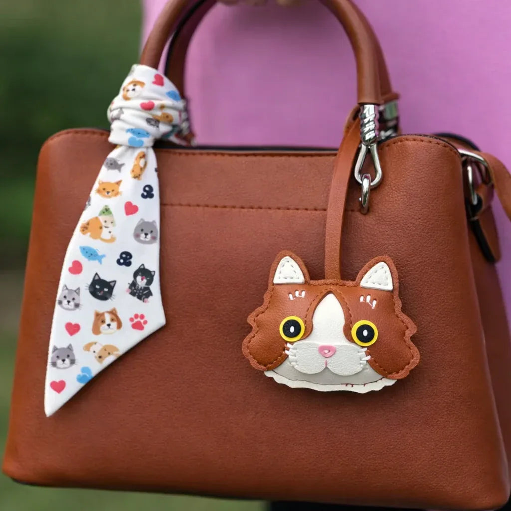 Tan Whiskered Heirloom Leather Cat Charm on  purse with scarf.