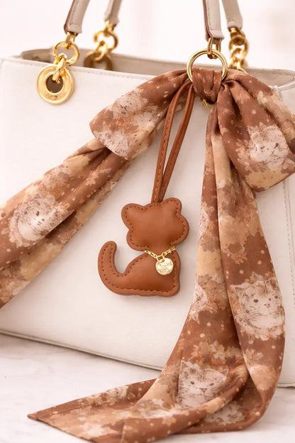 Brown Cozy Kitty Handmade Leather Kitten Bag Charm with leather strap on a white purse with scarf.