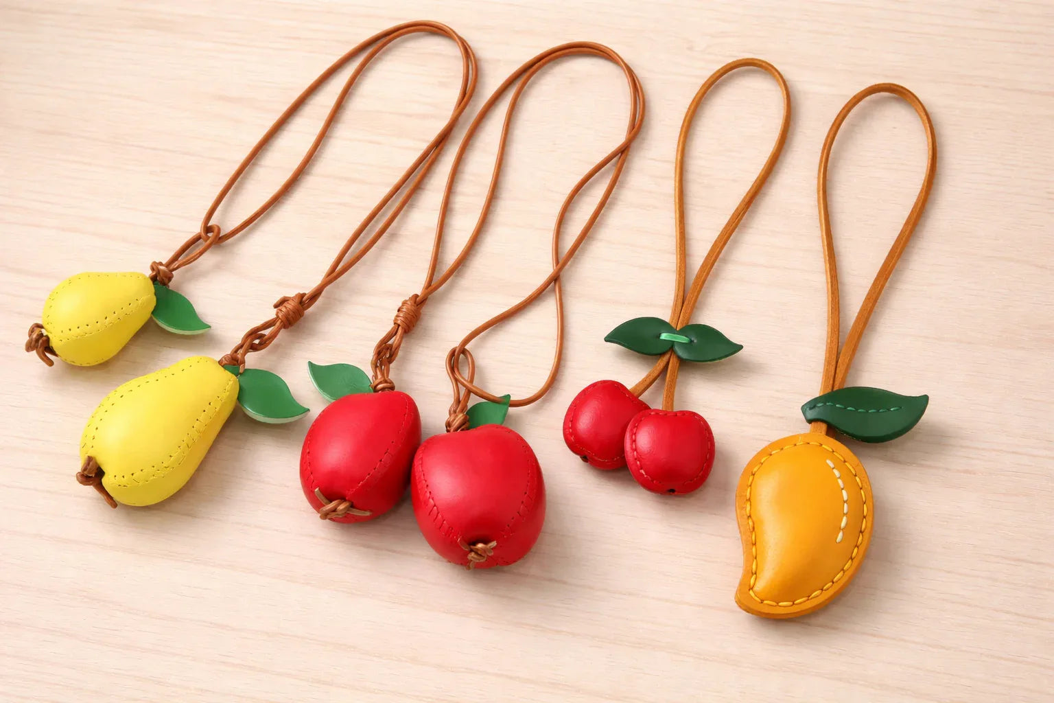 4 separate Orchard Luxe Leather Fruit Bag Charms with leather strap on table. 