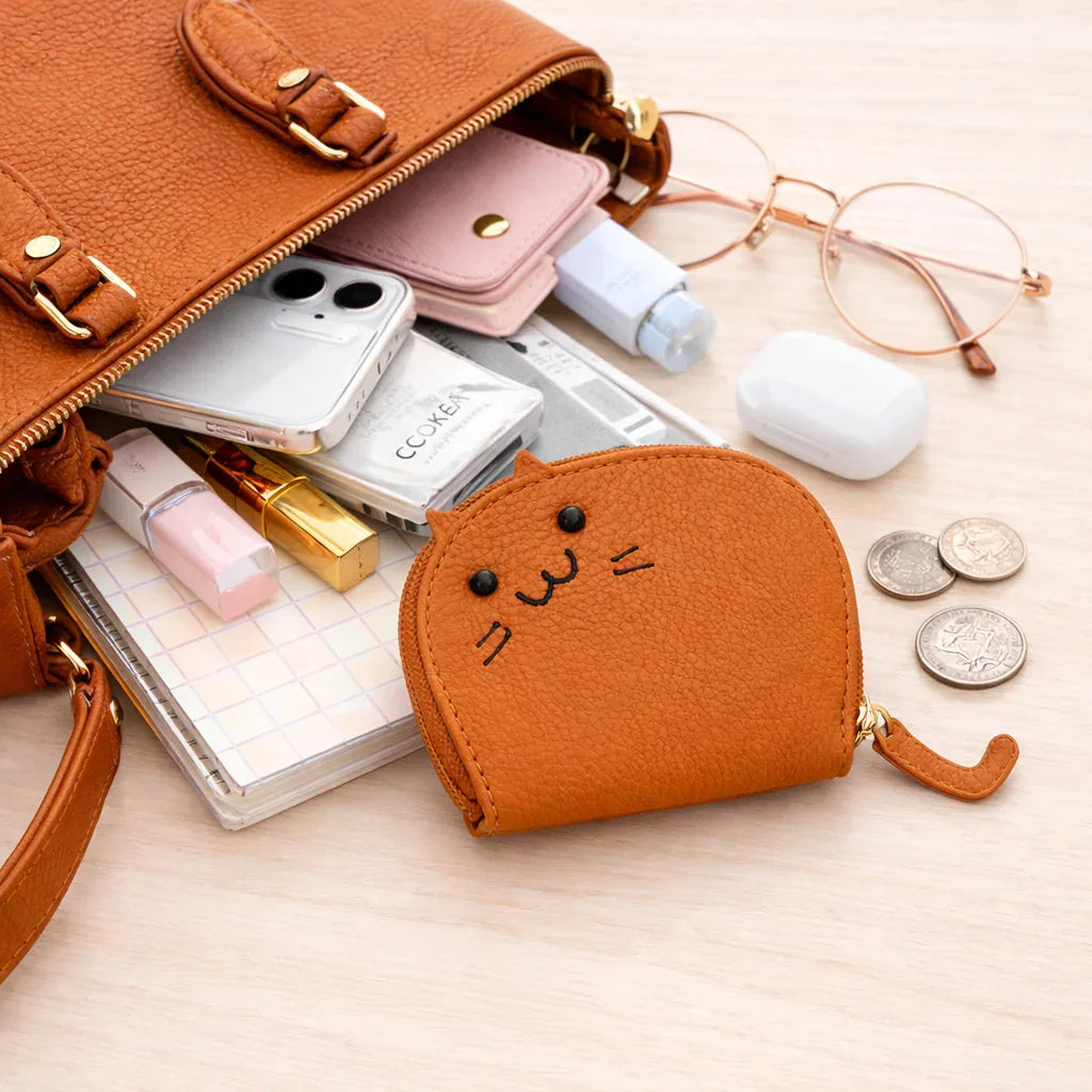 Small cat-shaped coin purse on table next to larger purse to show the compact size of the cardholder