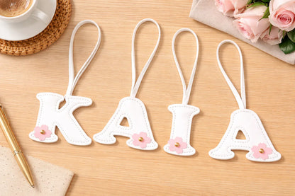 Initials in Bloom Alphabet Bag Charms spelling KAIA with leather strap on table with coffee and flowers. 