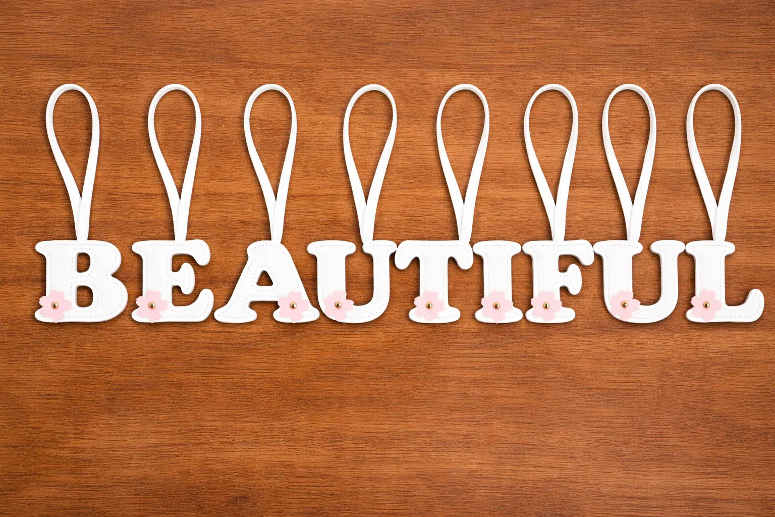 Initials in Bloom Alphabet Bag Charms spelling BEAUTIFUL with leather strap on table. 