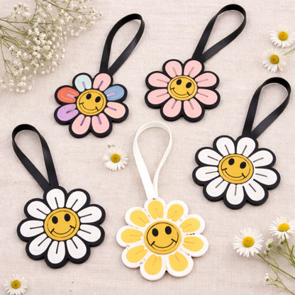 5 different colored Smiles in Bloom Daisy Bag Charms in a circle on table with flowers. 