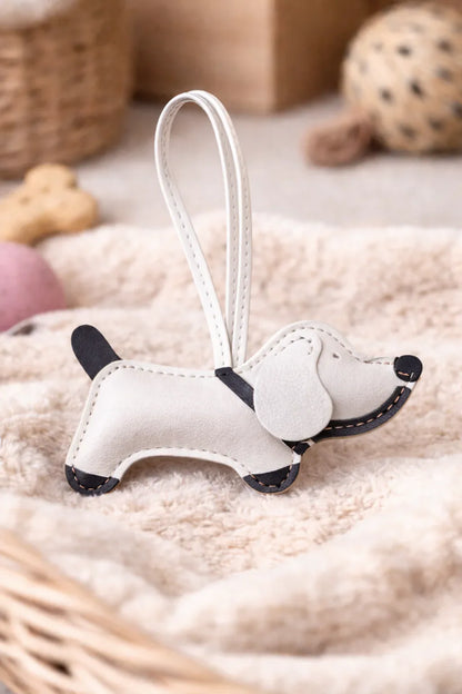 Chic White Leather Dachshund Bag Charm  with leather strap sitting on blanket. 