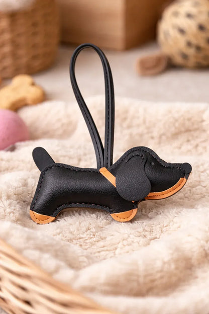 Chic Black Leather Dachshund Bag Charm  with leather strap sitting on blanket. 