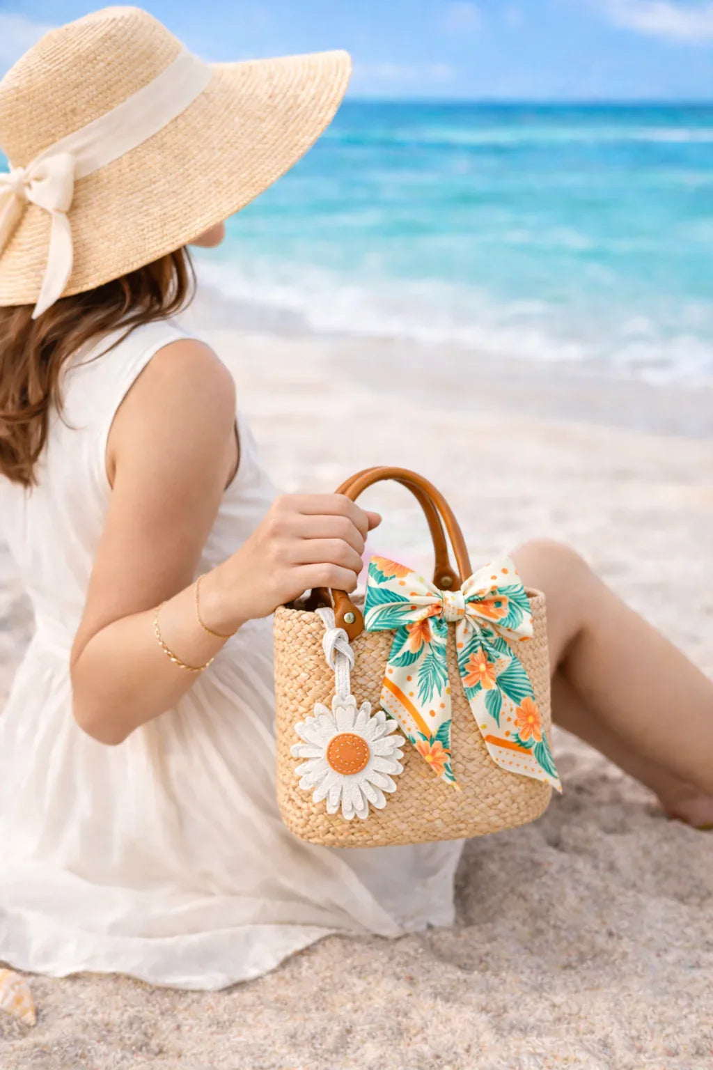 Woman holding straw bag with Sunlit Daisy Leather Bag Charm  and scarf at beach.