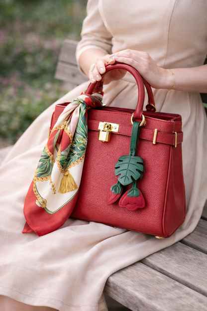 Women on a park bench holding a red luxury bag with a Red Monstera Bloom Leather Bag Charm and scarf. 