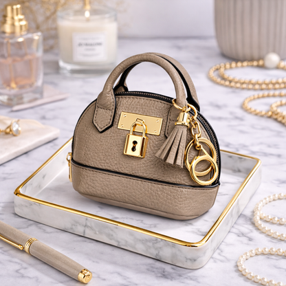 Petite beige Leather Purse Lock & Key Bag Charm  with key ring and zipper on marble surface with pen and pearls. 