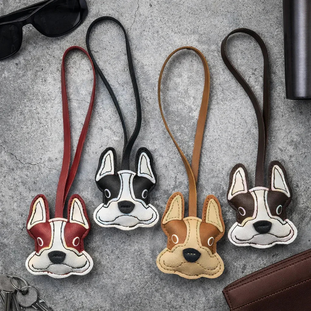 4 different colored Bulldog Leather Bag Charms with lather strap on table with keys, wallets and sunglasses. 