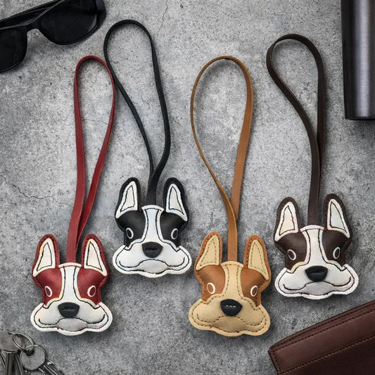 4 different colored Bulldog Leather Bag Charms with lather strap on table with keys, wallets and sunglasses. 