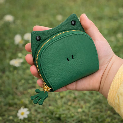 Handcrafted green leather frog-shaped card holder with a smiling face and gold zipper held in hand to show size.