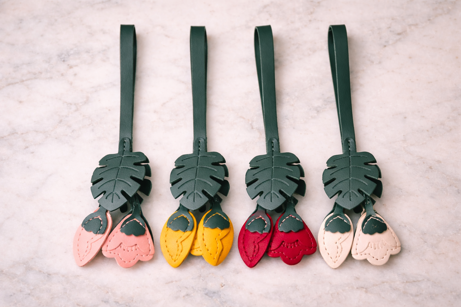 4 different colored Monstera Bloom Leather Bag Charms on marble table. 