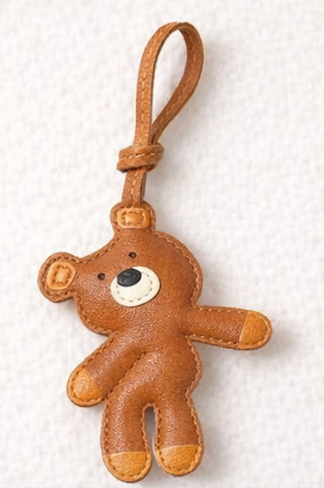 Brown teddy bear leather bag charm on a white textured background