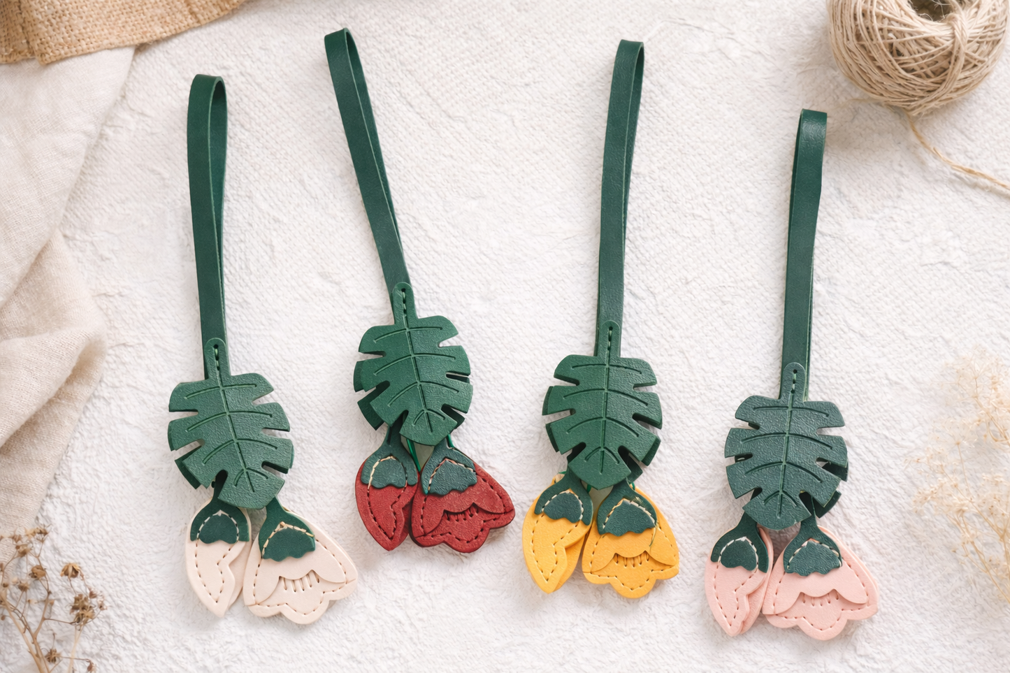 4 different colored Monstera Bloom Leather Bag Charms on white table cloth. 