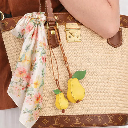 Woman holding a Pear Orchard Luxe Leather Fruit Bag Charms with leather strap on straw luxury bag. 
