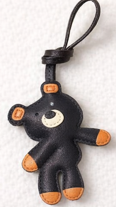 Black plush bear leather bag charm with orange accents on a white background