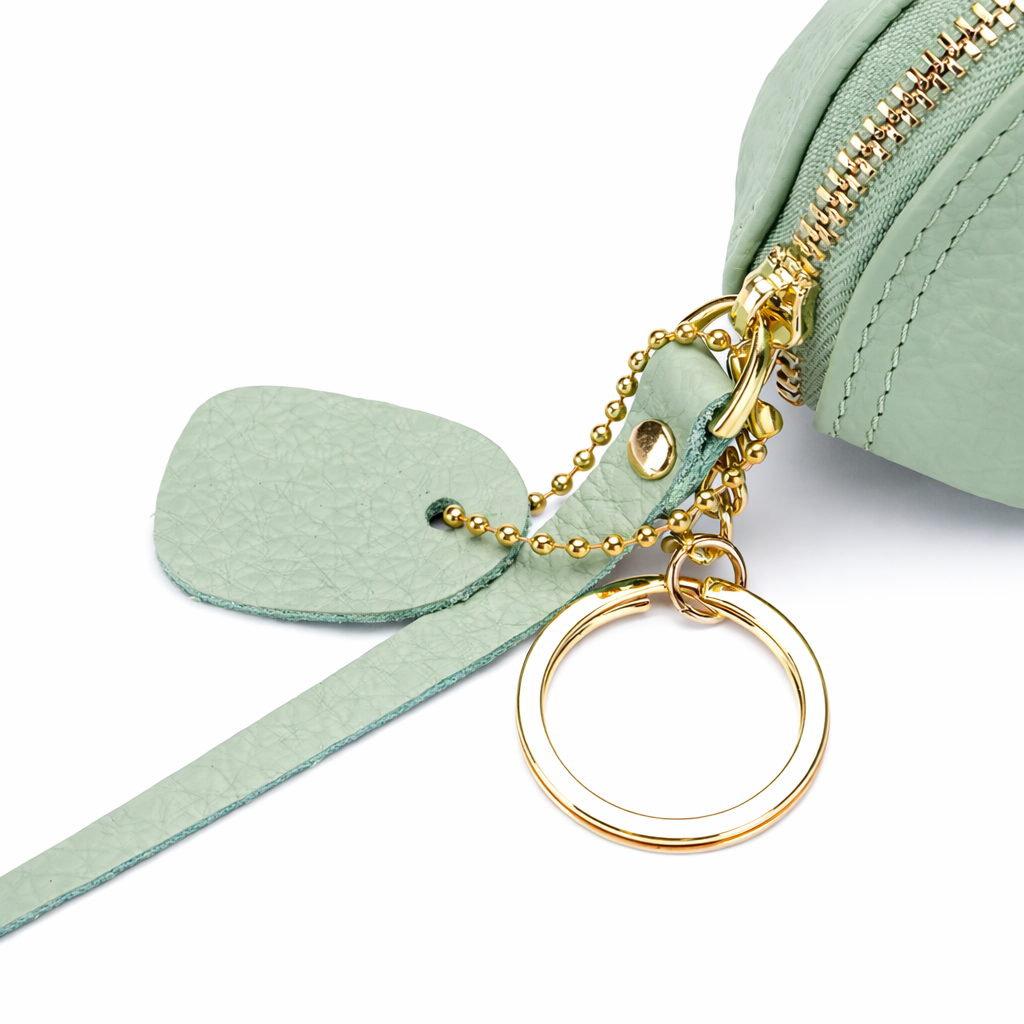 Close up of zipper and key ring of a green leather mouse purse with gold zipper and keychain on a white background.