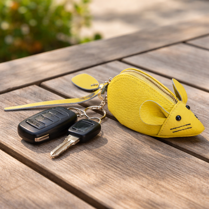 Handcrafted yellow  leather mouse-shaped coin purse with round ears and a secure zipper with keys hooked to key ring sitting on table. 