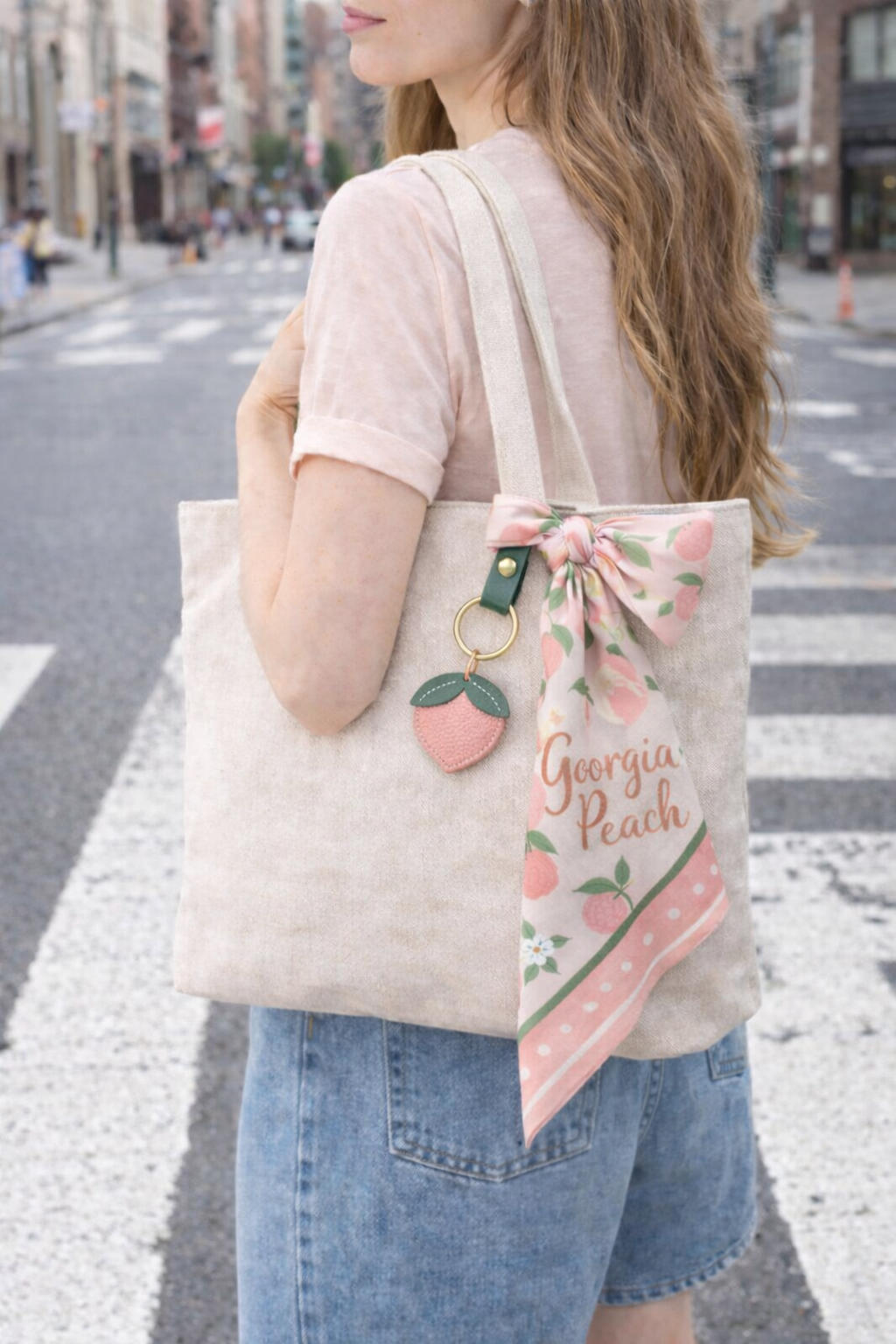 Woman walking in city with tote bag with Little Orchard Peach Fruit Bag Charm with leather strap connected. 