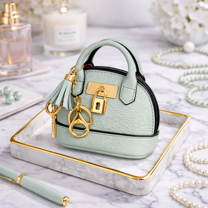 Petite green Leather Purse Lock & Key Bag Charm  with key ring and zipper on marble surface with pen and pearls. 