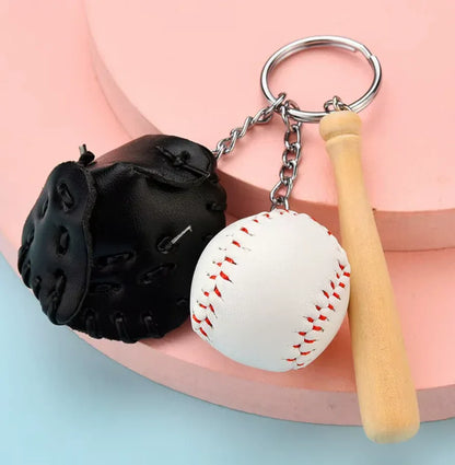 Baseball, black glove and bat keychain on a tan table. 