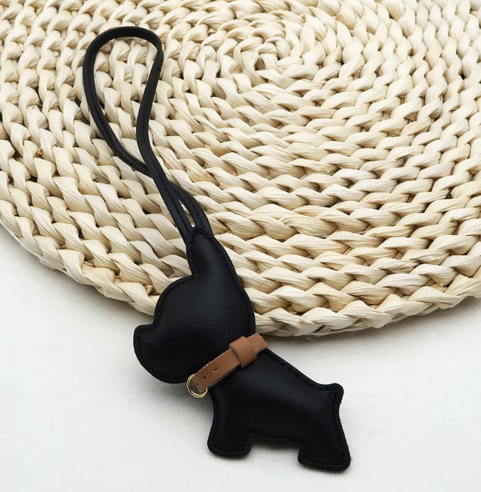Black Pocket Puppy Leather Bag Charm  with collar on a straw mat. 