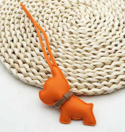 Orange Pocket Puppy Leather Bag Charm  with collar on a straw mat. 