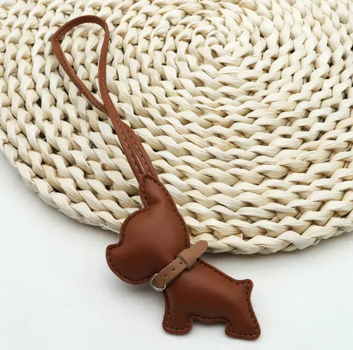 Ruby colored Pocket Puppy Leather Bag Charm  with collar on a straw mat. 