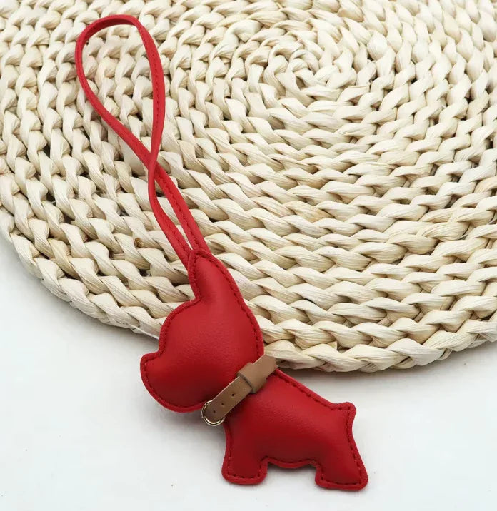 Red Pocket Puppy Leather Bag Charm  with collar on a straw mat. 