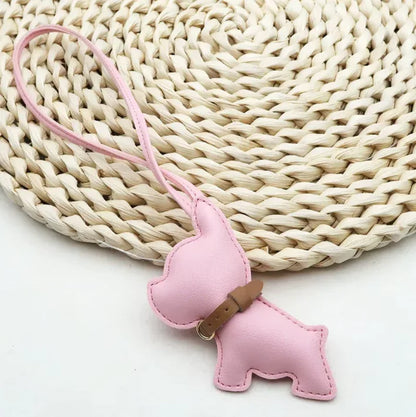 Pink Pocket Puppy Leather Bag Charm  with collar on a straw mat. 