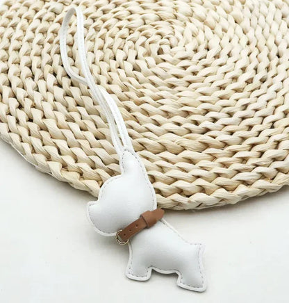 White  Pocket Puppy Leather Bag Charm  with collar on a straw mat. 