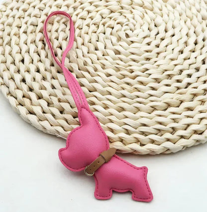 Pink Pocket Puppy Leather Bag Charm  with collar on a straw mat. 