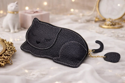 Catnap Cuties sleeping cat leather coin purse in Black with a zipper closure with tail sitting on table.