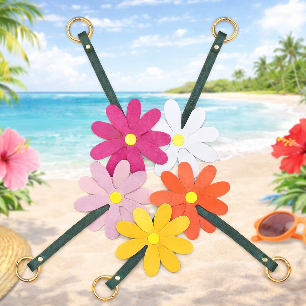 5 different colored Petal Pop Bag Charms with leather strap and brass ring in a circle with beach background. 