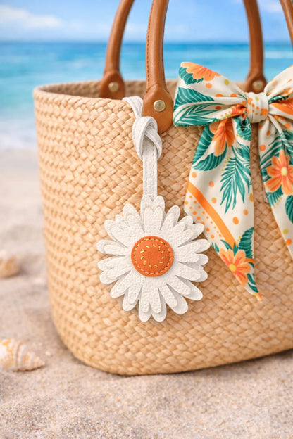 Sunlit Daisy Leather Bag Charm  with leather strap on straw beach bag at beach. 