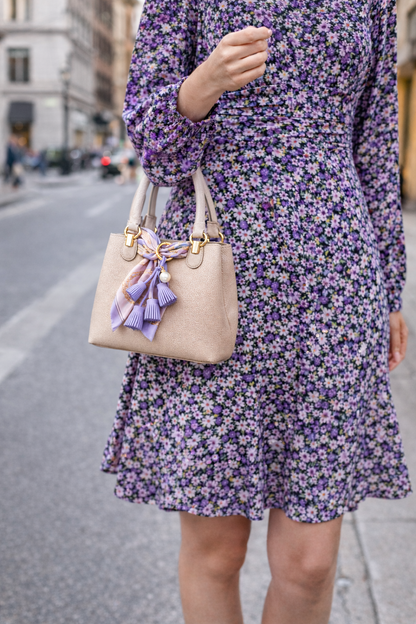 woman walking in city holding white purse with Blue Suede & Pearl Tassel Bag Charm with pearl accent on brass key ring. 