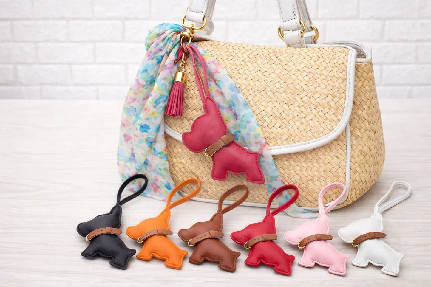6 different colored Pocket Puppy Leather Bag Charms  with collar in a row in front of a straw bag.