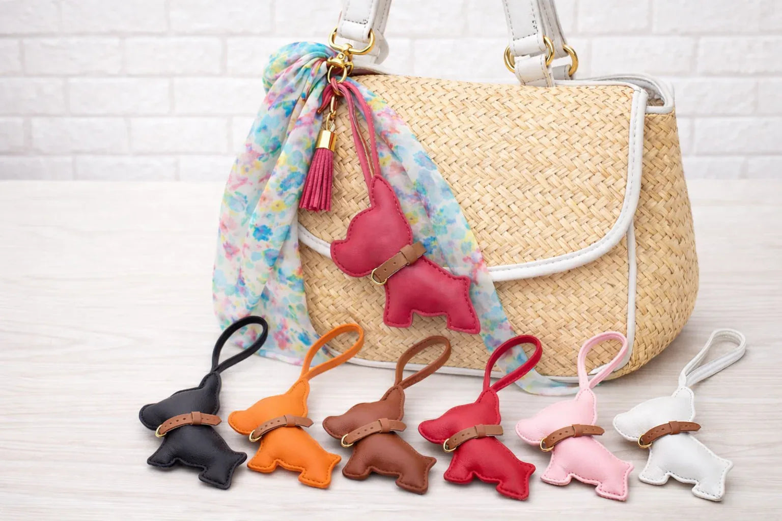 6 different colored Pocket Puppy Leather Bag Charms  with collar in a row in front of a straw bag.
