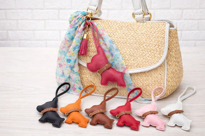 6 different colored Pocket Puppy Leather Bag Charms  with collar in a row in front of a straw bag.